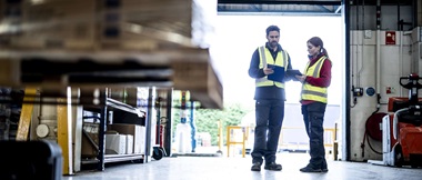 Deux travailleurs (un homme, une femme) sont debout dans une usine et examinent un document dans cette scène d'entrepôt de transport et de logistique.