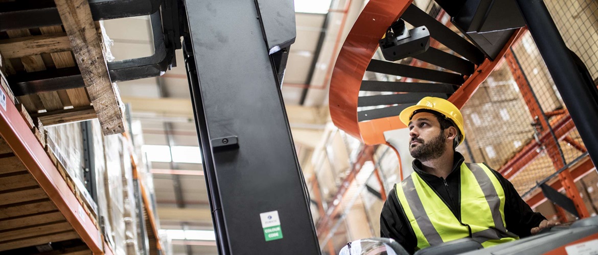 Een mannelijke fabrieksarbeider bedient een hoogwerker in een pakhuis in dit vervoer en logistiekbeeld