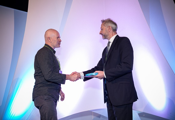 Two men stood shaking hands, with the man on the left accepting an award